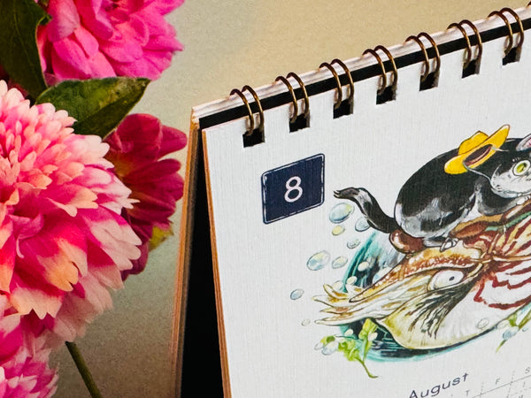 Calendar with a penguin illustration on a table next to pink flowers