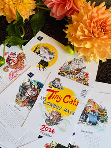 Calendar with cat illustrations and 'Tiny Cats in Cowboy Hats' text, surrounded by flowers.