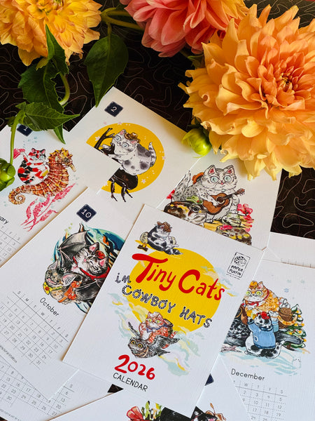 Calendar with cat illustrations and 'Tiny Cats in Cowboy Hats' text, surrounded by flowers.