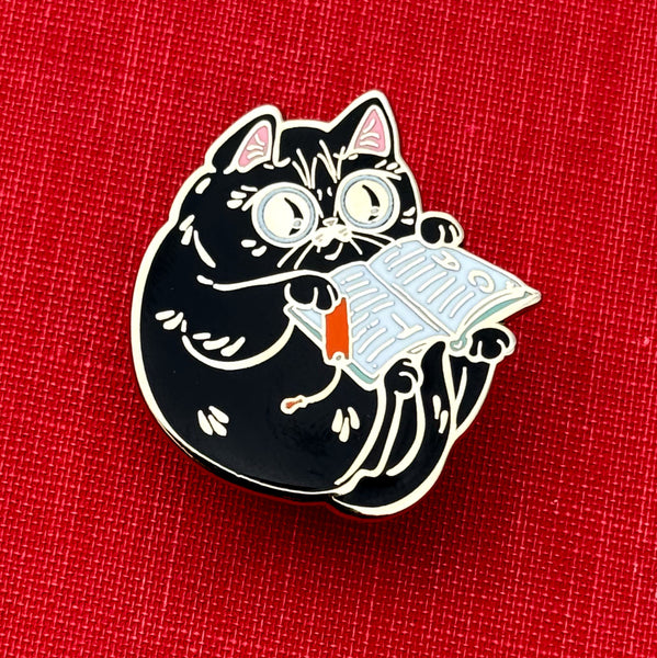 Black cat reading a book enamel pin on a red background